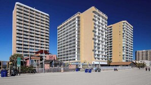 Un hotel frente a la playa con varios edificios altos, un paseo marítimo y un restaurante a la orilla del mar.