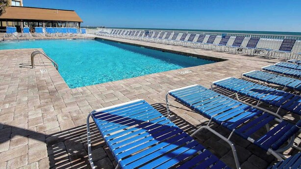 Zona de piscina con sillones reclinables azules y vista despejada al océano.