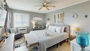 Une chambre d’hôtel comprenant un lit, des tables de chevet, un bureau, une chaise, un ventilateur de plafond et une fenêtre avec des stores.