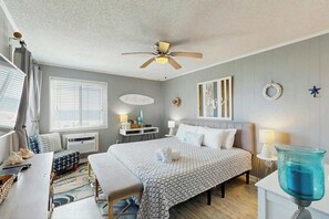 Ein Hotelzimmer mit Bett, Nachttischen, Schreibtisch, Stuhl, Deckenventilator und einem Fenster mit Jalousien.