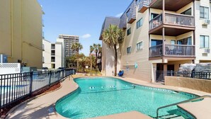 Un espace piscine avec une piscine à l’eau d’un bleu limpide, entourée d’une clôture, et jouxtant un immeuble à plusieurs étages doté de balcons.