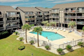 A multi-story hotel with a central swimming pool surrounded by lounge chairs and palm trees. - Shipwatch Pointe I E-308 (Myrtle Beach)