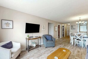 A living room with a flat-screen TV, a sofa, a chair, a coffee table, and a dining area with a table and chairs. - Shipwatch Pointe I E-308 (Myrtle Beach)