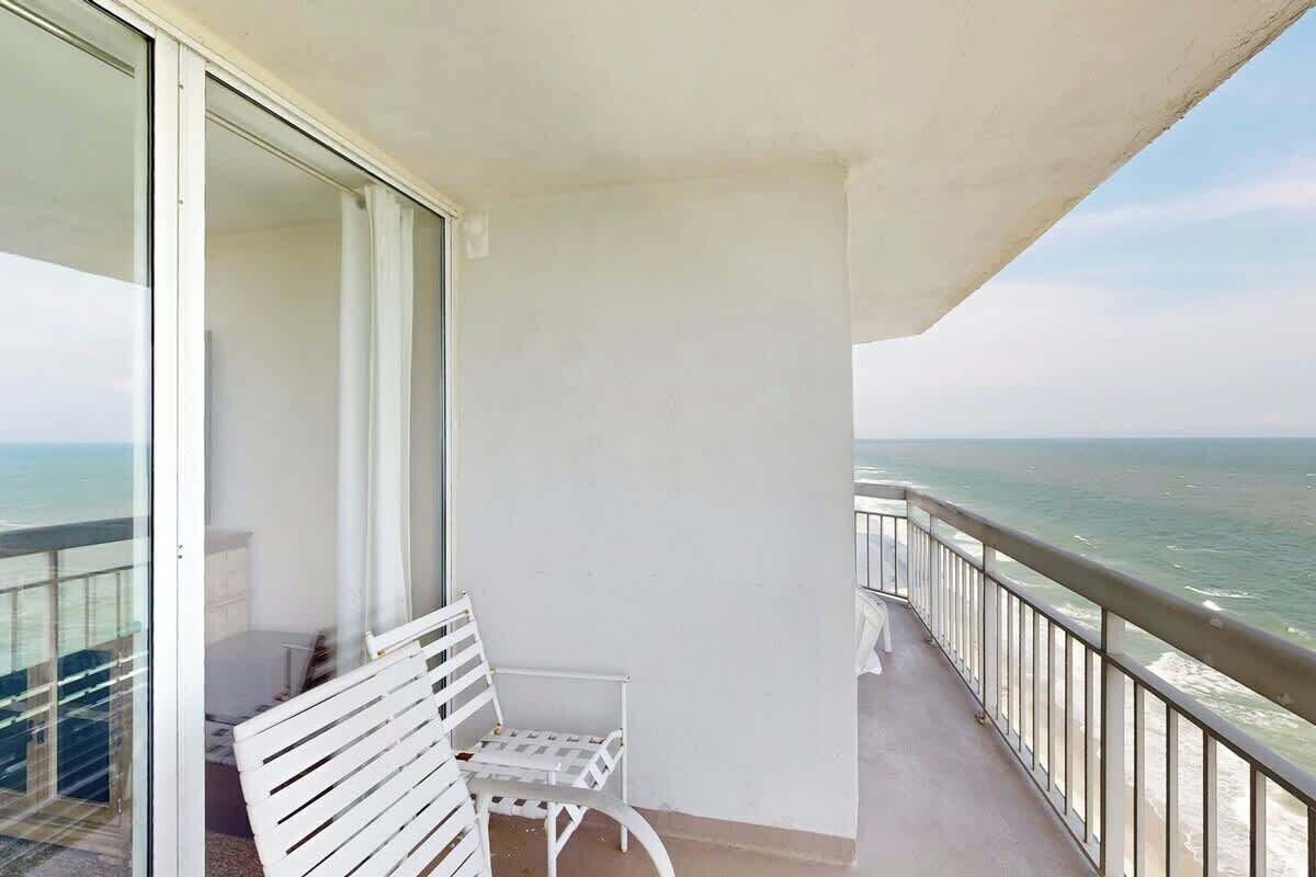 A balcony with a white chair and a table, overlooking the sea.