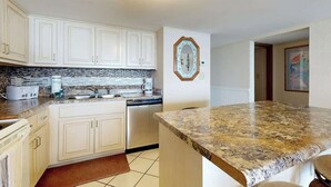 A kitchen with white cabinets, a granite countertop, and a backsplash. - Water's Edge Resort 1501 (Murrells Inlet)