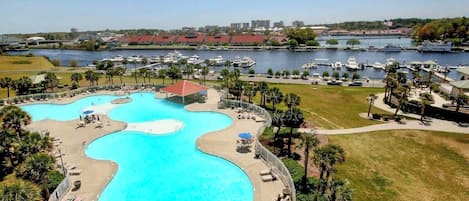 A large, curved swimming pool with lounge chairs and umbrellas, surrounded by a grassy area and palm trees.