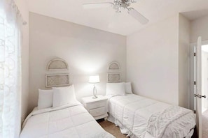 Ein Zimmer mit zwei Betten, einem Nachttisch mit Lampe und einem Deckenventilator.