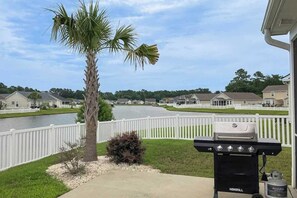 Ein Garten mit Grill, einer Palme und Blick auf einen See und Häuser.