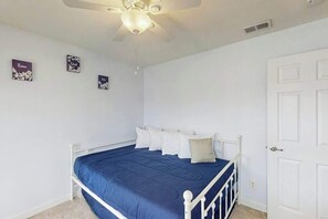 Ein Schlafzimmer mit Bett, weißen Wänden, Deckenventilator und Tür.