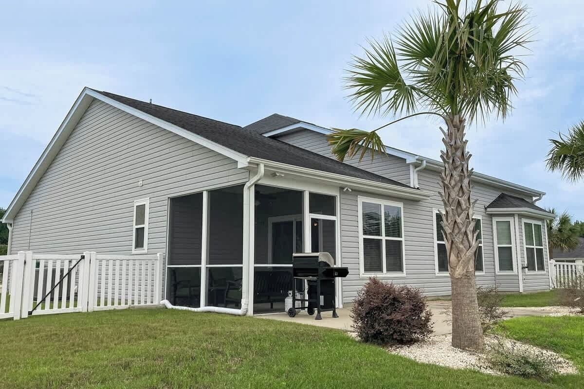 A single-story house with a covered porch, a screened window, and a palm tree in the yard.