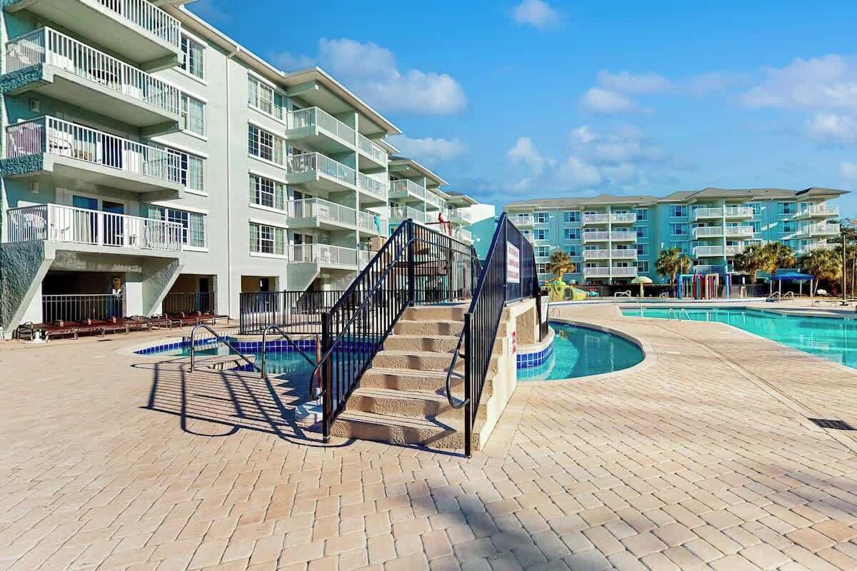 A hotel with multiple balconies, a swimming pool, and a brick-paved area.
