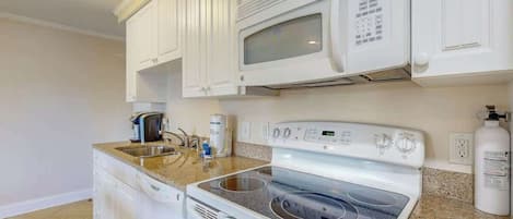 A kitchen with white cabinets, a microwave, a stove, and a coffee maker.