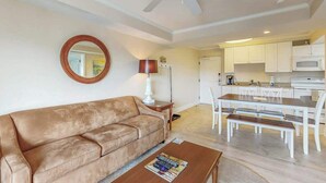 A living room with a sofa, coffee table, and a dining area with chairs and a table. - Summerhouse at Litchfield (Pawleys Island)