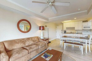A living room with a sofa, coffee table, and a dining area with chairs and a table. - Summerhouse at Litchfield (Pawleys Island)