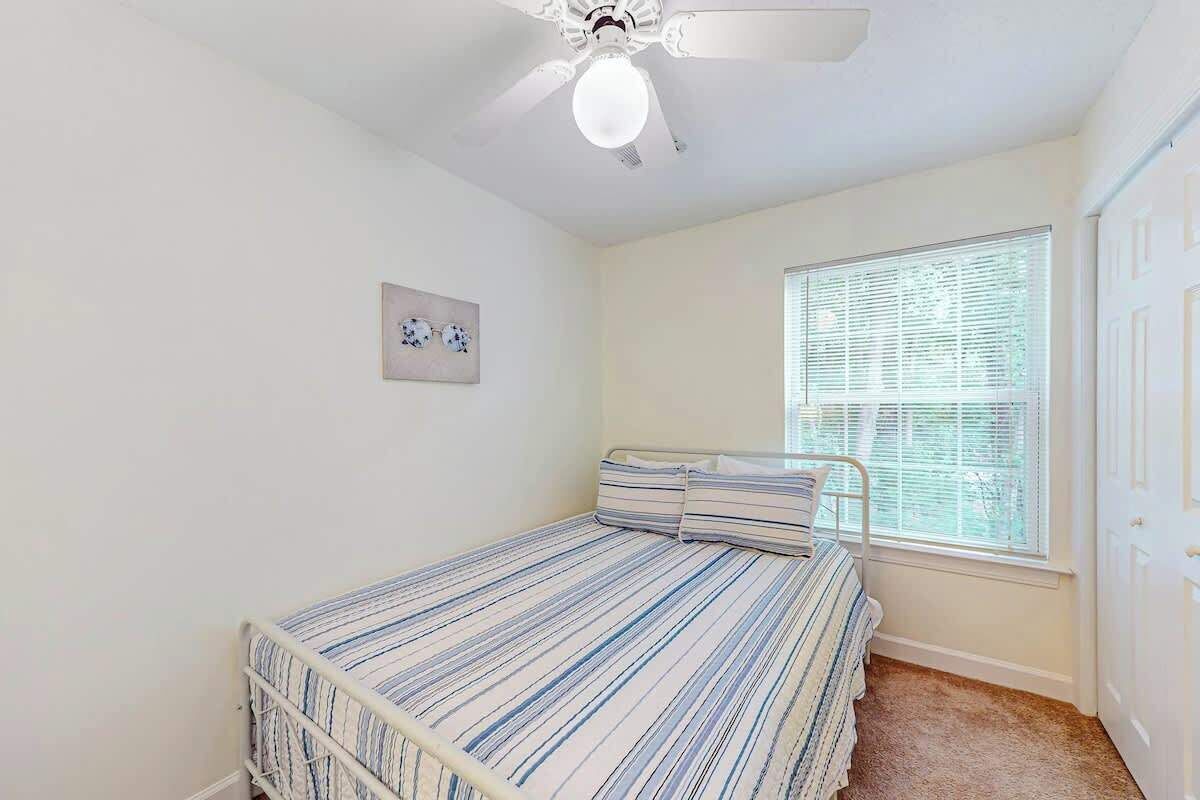 Un dormitorio con una cama individual, ventilador de techo, ventana con persianas y una puerta.