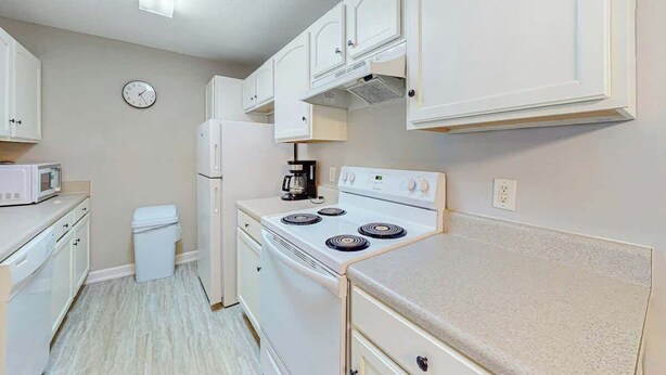 A compact kitchen with white cabinets, a stove, a microwave, and a refrigerator. - Seascape Beach Retreat (Murrells Inlet)