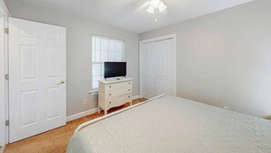 A bedroom with a bed, a dresser, a television, and two doors. - Seascape Beach Retreat (Murrells Inlet)