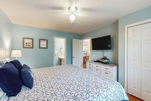 Ein Schlafzimmer mit Bett, Deckenventilator, Kommode, Fernseher und einer Tür.