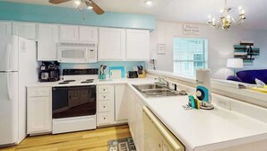A modern kitchen with white cabinets, a microwave, stove, and a ceiling fan. - Anchors Away Unit 7G (Myrtle Beach)