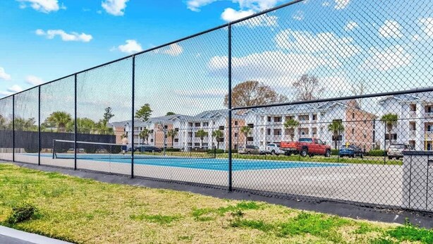 A fenced outdoor area with a swimming pool, adjacent residential buildings, and a clear sky. - Anchors Away Unit 7G (Myrtle Beach)