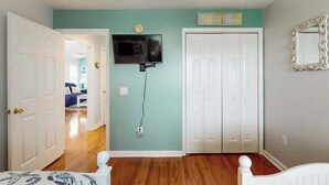 A room with a bed, a television mounted on the wall, a white door, and a white closet. - Anchors Away Unit 7G (Myrtle Beach)