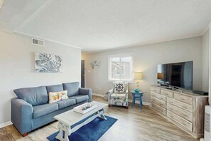 Ein Wohnzimmer mit Sofa, Couchtisch, Fernseher und einem Sessel mit Kopfkissen in Form eines Schiffsrades.