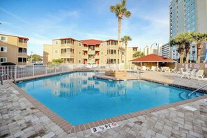 A swimming pool with a 3 1/2 ft depth marker, surrounded by a white fence, with a palm tree and a covered seating area with lounge chairs. - Steps to the Beach Home (North Myrtle Beach)