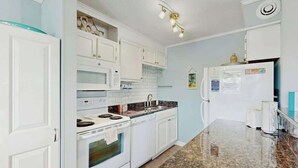 Una cocina con armarios blancos, encimera de granito, estufa, microondas y refrigerador.