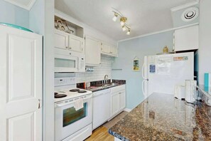A kitchen with white cabinets, a granite countertop, a stove, a microwave, and a refrigerator. - Steps to the Beach Home (North Myrtle Beach)