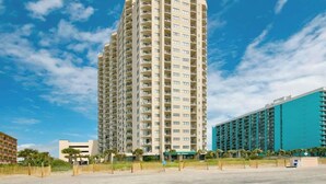 A high-rise hotel with multiple balconies, a flat roof, and a large parking area. - Sunrise at the Beach (Myrtle Beach)