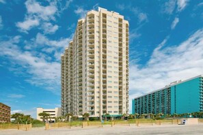 A high-rise hotel with multiple balconies, a flat roof, and a large parking area. - Sunrise at the Beach (Myrtle Beach)