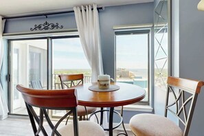 A room with a dining table and chairs, a window with a view, and a curtain. - Sunrise at the Beach (Myrtle Beach)
