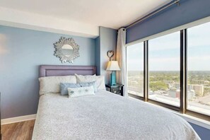 Ein Schlafzimmer mit einem großen Bett, einem Nachttisch, einem Spiegel und einem Fenster mit Blick auf die Stadt.