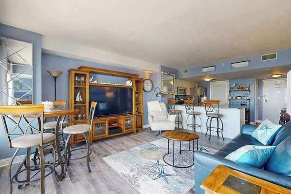 A living room with a television, bar stools, a sofa, and a kitchen area in the background. - Sunrise at the Beach (Myrtle Beach)
