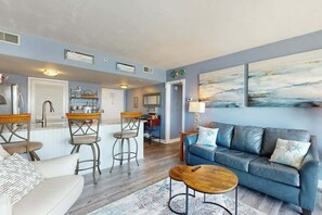 A living room with a blue sofa, two bar stools, a coffee table, and a painting on the wall. - Sunrise at the Beach (Myrtle Beach)