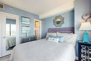 A bedroom with a bed, a mirror, a lamp, and artwork on the wall. - Sunrise at the Beach (Myrtle Beach)