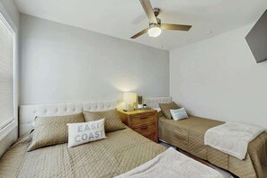 A bedroom with two beds, a ceiling fan, a bedside table with a lamp, and a wall-mounted TV. - Palmetto Dunes Unit 303 (North Myrtle Beach)