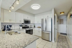 A modern kitchen with white cabinets, stainless steel appliances, and a granite countertop. - Palmetto Dunes Unit 303 (North Myrtle Beach)
