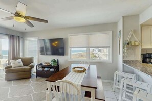 A modern living room with a dining area, a ceiling fan, a TV, and a view of the beach. - Palmetto Dunes Unit 303 (North Myrtle Beach)