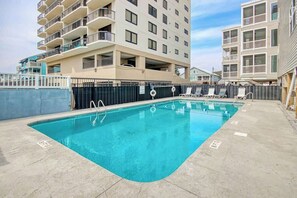 A swimming pool with a concrete deck, surrounded by a fence, and adjacent to a multi-story building with balconies. - Palmetto Dunes Unit 303 (North Myrtle Beach)