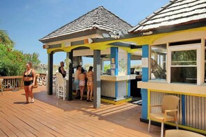 Ein überdachter Außenbereich mit Holzdeck, einem kleinen Kiosk und einer Sitzgelegenheit mit Stühlen.