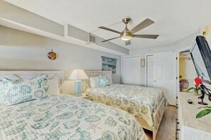 Ein Schlafzimmer mit zwei Betten, einem Deckenventilator, einem Nachttisch mit Lampe sowie einem Schreibtisch mit Computer und Dekoration.