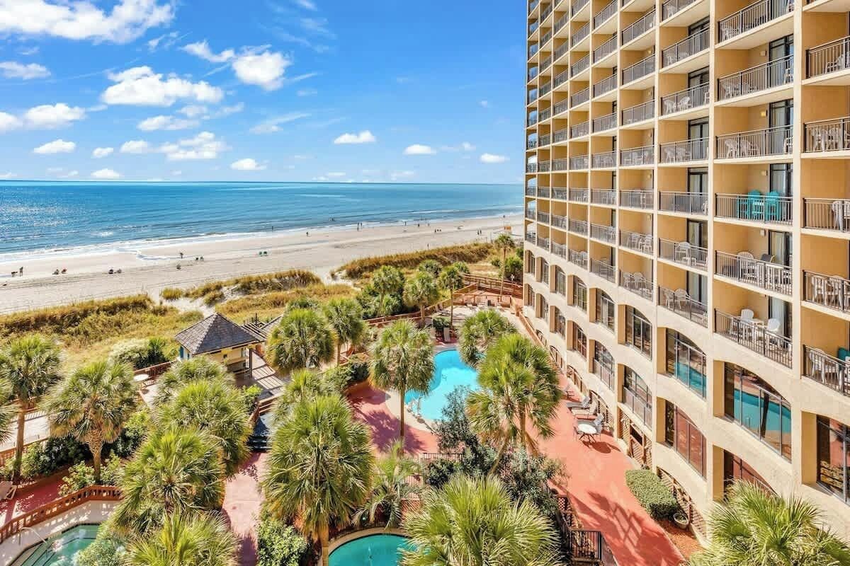 A hotel with a pool, beach view, and multiple balconies.