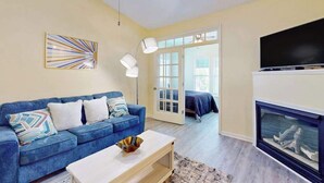 A living room with a blue sofa, a white coffee table, a fireplace, and a television. - Savannah Shores Unit 12 (Myrtle Beach)