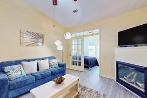 Ein Wohnzimmer mit blauem Sofa, weißem Couchtisch, Kamin und Fernseher.