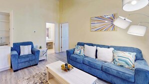 A living room with a blue sofa, a coffee table, and a painting on the wall. - Savannah Shores Unit 12 (Myrtle Beach)