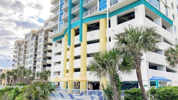 A multi-story hotel with balconies, a pool area, and palm trees. - This is It 2 BR Condo (North Myrtle Beach)