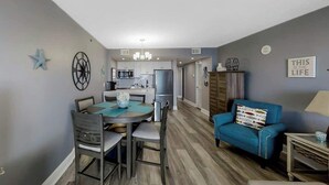 A modern living room with a dining area, kitchen in the background, and a blue sofa. - This is It 2 BR Condo (North Myrtle Beach)