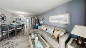 A modern living room with a dining area, kitchen, and a large framed picture on the wall. - This is It 2 BR Condo (North Myrtle Beach)