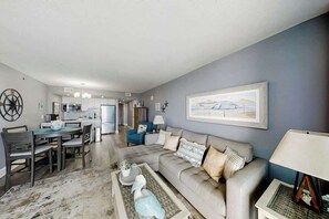 A modern living room with a dining area, kitchen, and a large framed picture on the wall. - This is It 2 BR Condo (North Myrtle Beach)